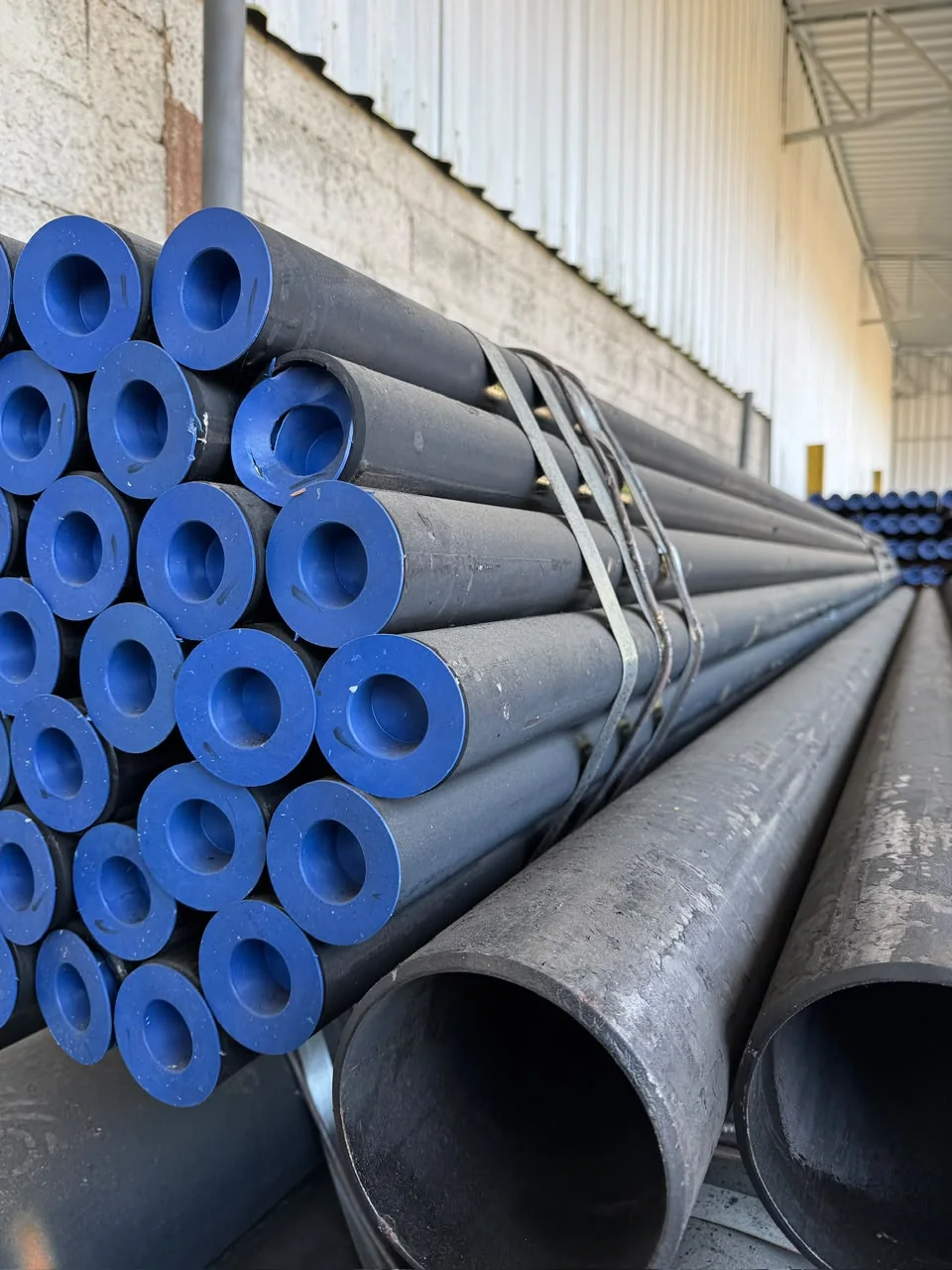 Tubos de aço carbono empilhados com tampas de proteção azuis